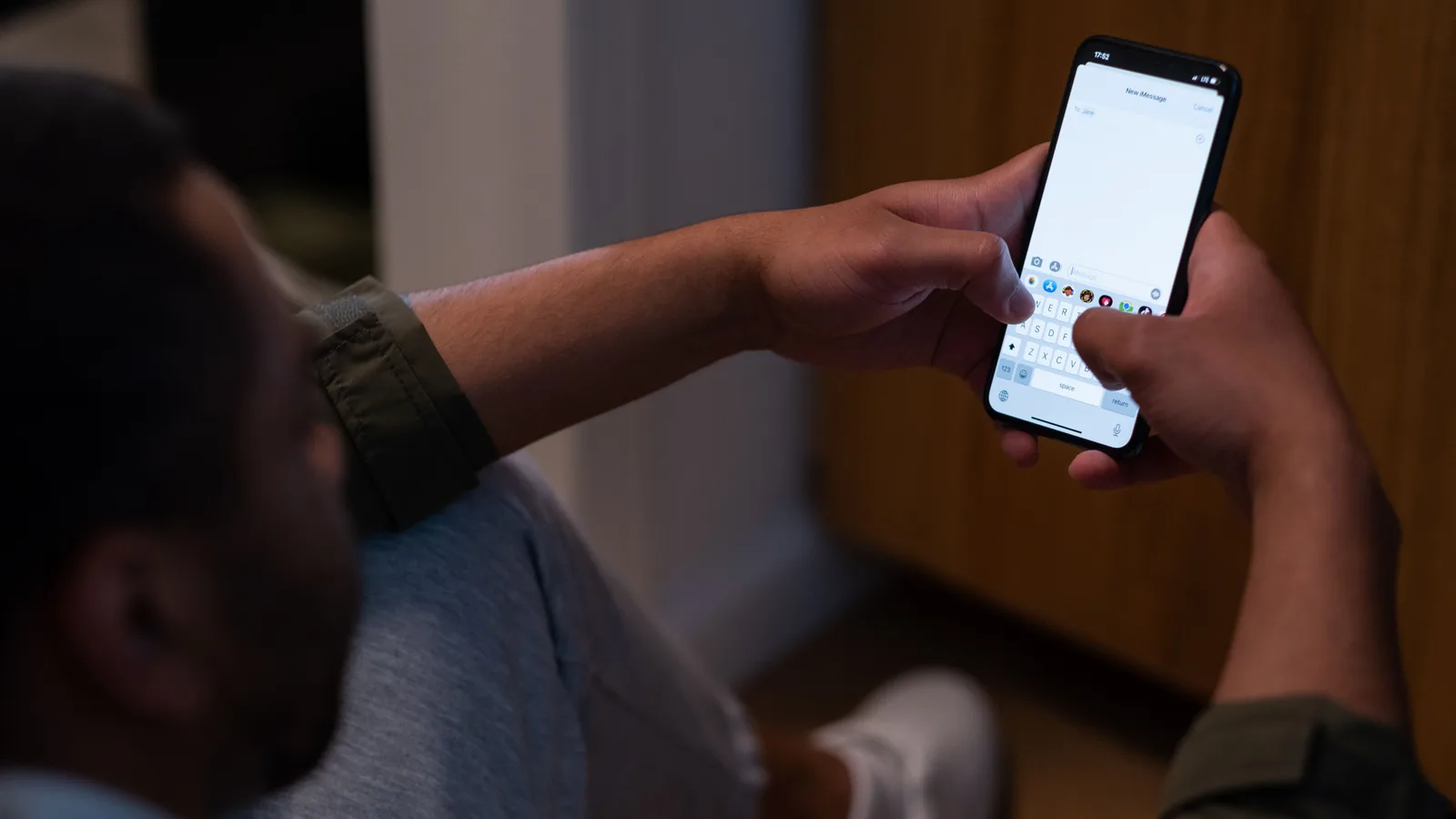 A man in a dim room at night typing a message on his phone