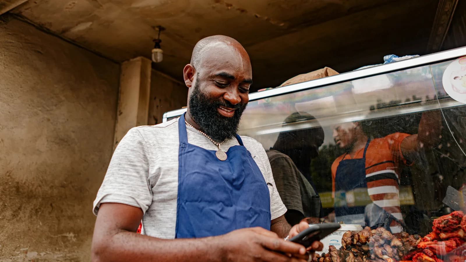 Smiling food stall owner reading a message on his phone while standing at his grill