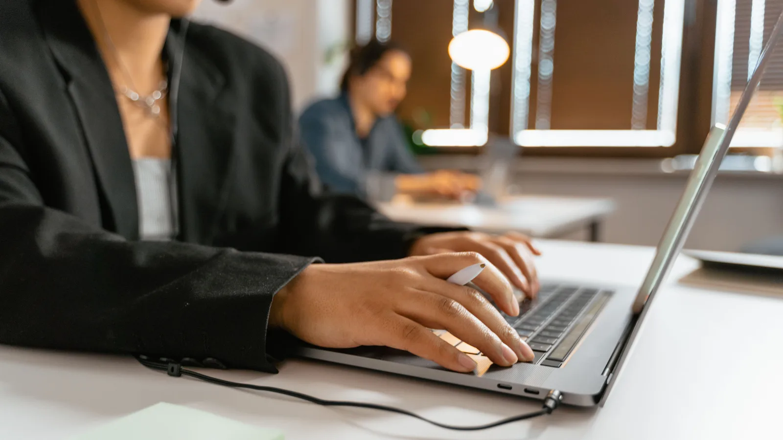 Support agent wearing a headset and typing on a laptop while a colleague works nearby